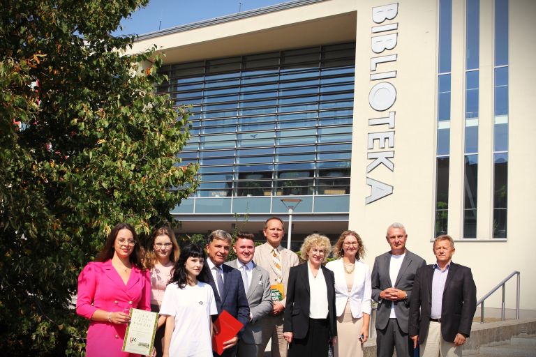 Grupa uczestników spotkania pozuje do wspólnego zdjęcia przed budynkiem biblioteki